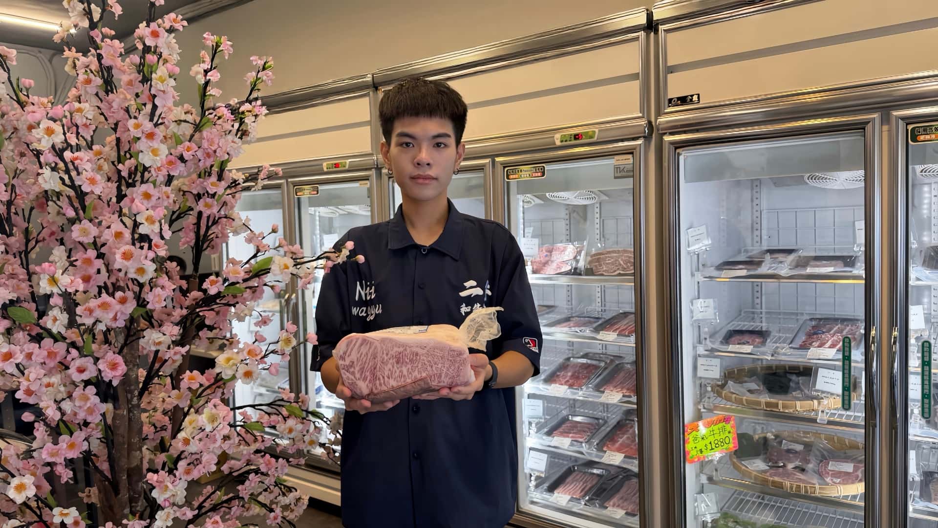 雙手鎖起的職人溫度:二井和牛如何在AI搜尋時代找到頂級生鮮的第二個入口 二井員工手捧和牛肉品,身後為店內冷藏展示櫃與熱銷燒肉牛排商品。圖:二井和牛肉品提供